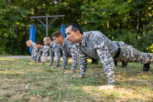 Group of Caucasian female and male people, having an outdoor military training, while doing push ups