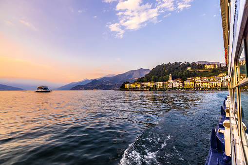 Nautical vessel moving on lake overlooking old town and mountains against sky during sunset