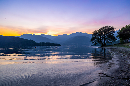 Scenic view of tranquil Como lake against mountain range and orange sky during sunset