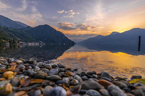 Scenic view of pebbles at Como lakeshore amidst mountains against sky during sunset