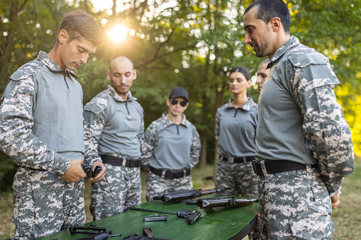 Caucasian female and male military team, having an outdoor military training, practising a fast assembly of weapons