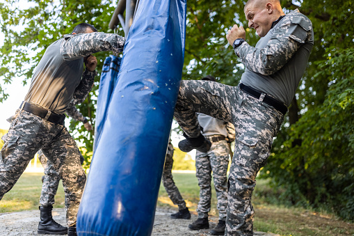 Caucasian female and male military team, having an outdoor military training, while punching the punching bag