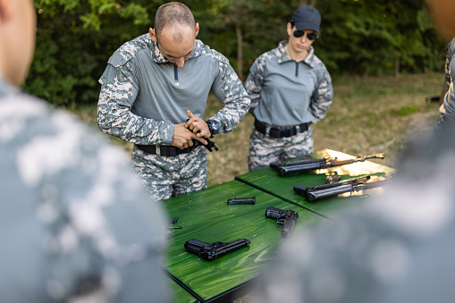 Caucasian female and male military team, having an outdoor military training, practising a fast assembly of weapons