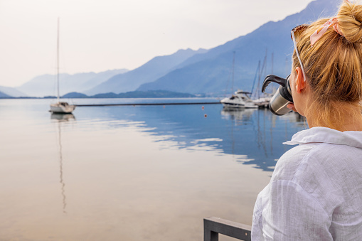 Female tourist drinking coffee while looking at nautical vessels in calm lake against mountain