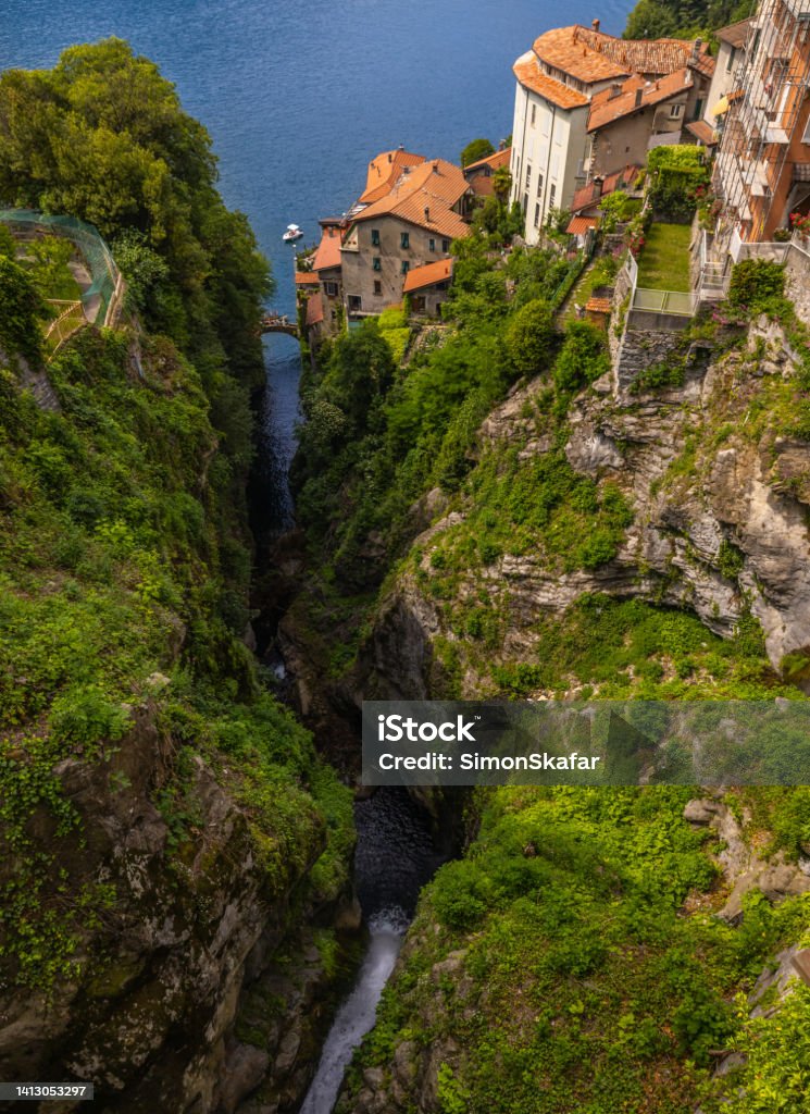 High angle view of old houses on beautiful mountains against lake. Lake Como, Italy. Town of Nesso. Historic stone bridge. High angle view of old houses on beautiful mountains against famous lake in town Como - Italy Stock Photo