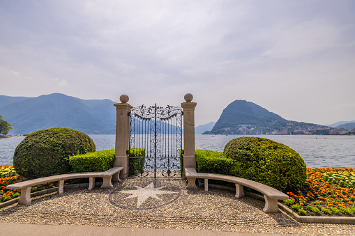 Closed gate of classical style public park with view of lake and mountains against sky