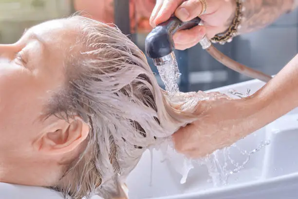 Professional hairstylist washes client's color hair with conditioner shampoo for washing after process of coloring hair in beauty salon. Shallow depth of field