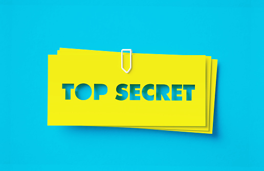 Top Secret written cut out yellow adhesive notes sitting on blue background. Horizontal composition with copy space.