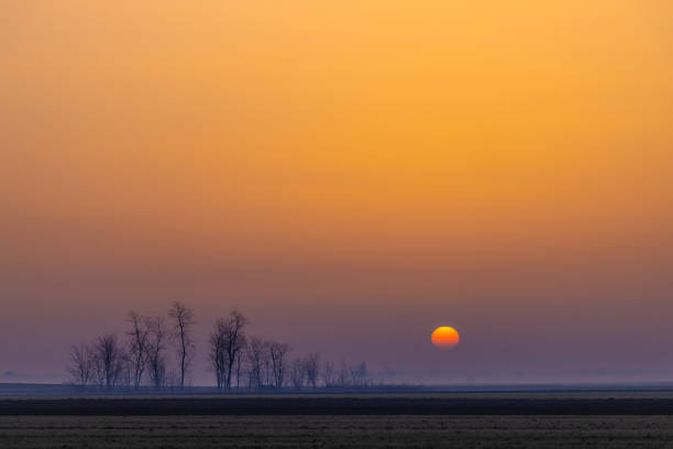 Scenic view of sun setting over dramatic rural landscape during foggy weather