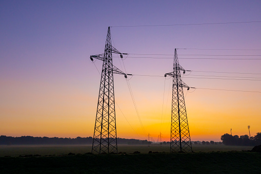 View of electricity pylons on field against clear orange sky during sunset