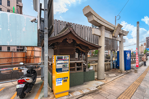 nagasaki, kyushu - december 12 2021: Hokora shrine called Ebisu Jinja with a torii gate dedicated to the fishermen Buddhist deity between a scooter parking and a vending machine along Nakashima river.