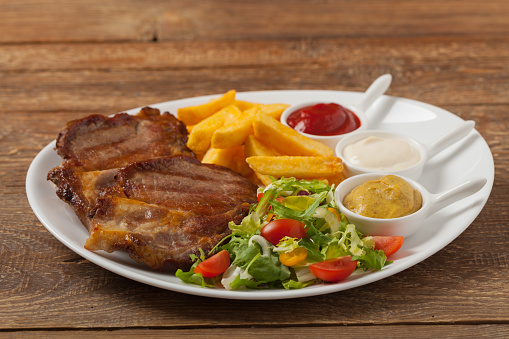 Grilled pork neck served with French fries and salad. Front view.