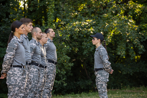 Group of Caucasian female and male people, having an outdoor military training, leaded by female sergeant