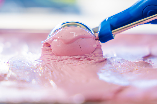 Strawberry ice cream with blue scoop in display freezer