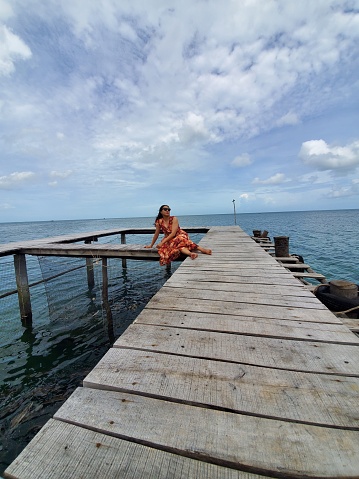 a young lady sitting on the wooden bridge at the beach