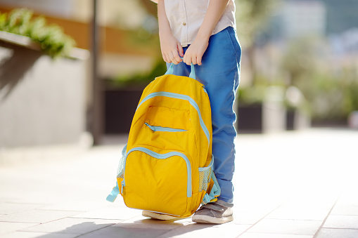 Little student with a backpack on the steps of the stairs of school building. Close-up of child legs, hands and schoolbag of boy standing on staircase of schoolhouse. Kids back to school concept.