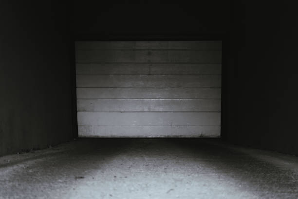 Dark underground garage with white door closed at the entrance. Entry tunnel to a basement parking lot