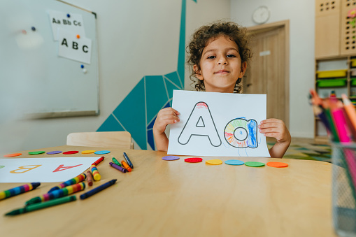 English lesson at elementary school or kindergarten. Girl learning the alphabet and colors coloring the letter A. Selective focus.
