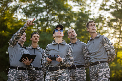 Caucasian woman from the military team, driving the drone while using drone remote control