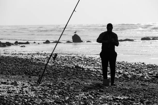un pêcheur et sa canne à pêcher en noir et blanc - catch of fish photos photos et images de collection