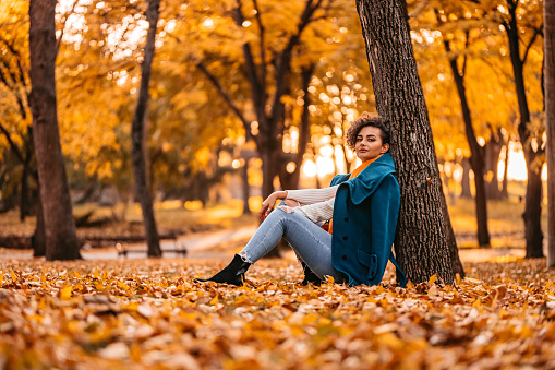 Profile of a beautiful young woman leaning on a tree in the park during autumn.