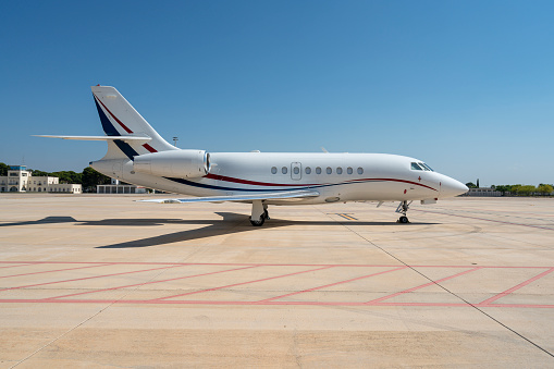 this is a black and white picture of a private luxury Jet at a airport. the jet or plane has it's landing gear and the jet is waiting to be boarded by passengers. the photo shows the jet's or plane's wing, pilot's cabin. in the background of the photo there are airplane hangers that house these private jets and commercial jets and planes. 