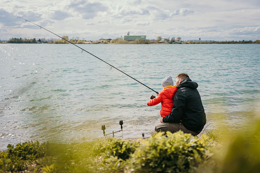 Father teaching his son reeling fishing rod at riverbank