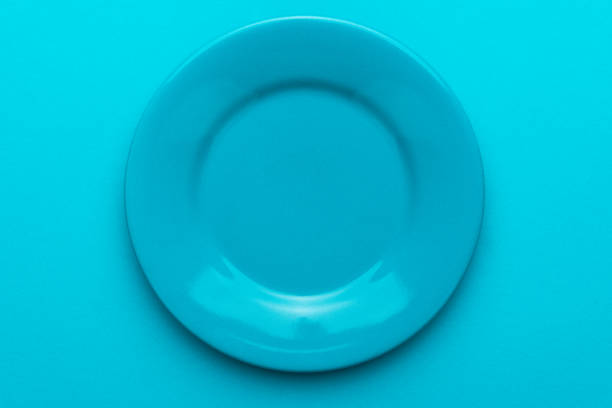 Top view photo of empty blue plate. Close up of round ceramic plate over turquoise blue background with copy space and central position. Minimalist photo of blank dish on blue table.