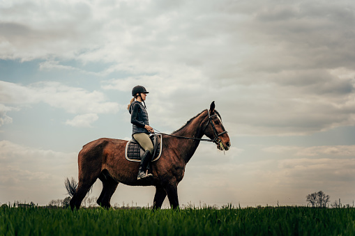 Side view of woman riding horse on grassy field against cloudy sky during equestrian event