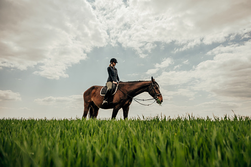 Full length of woman riding horse on grassy landscape against cloudy sky during equestrian event