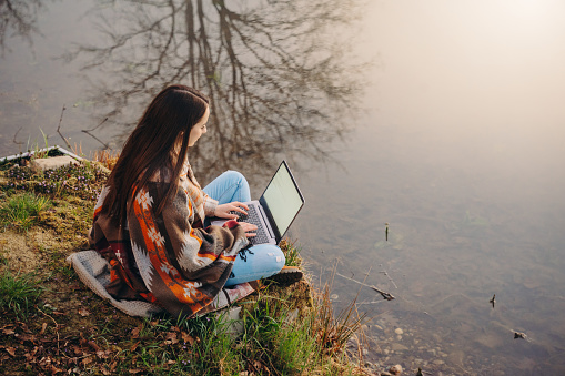 High angle view of young woman using laptop while sitting at lakeshore during foggy weather