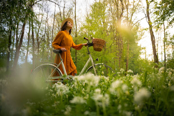 Young woman looking up while walking with bicycle amidst flowers in forest