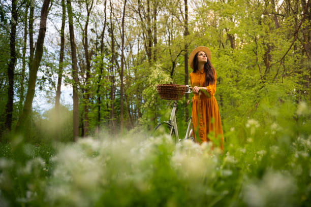 istock Woman wearing dress looking up while walking with bicycle in forest 1413072330