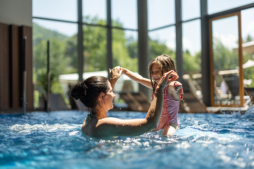 Young mother and her little daughter having fun in hotel swimming pool