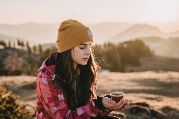 istock Young woman holding tea cup while sitting on top of mountain 1413075139