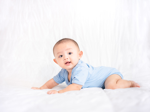Happy family, Cute Asian newborn baby wear blue shirt lying, crawling, play on white bed with laughing smile happy face. Little innocent infant adorable child in first day of life. Mother Day concept.