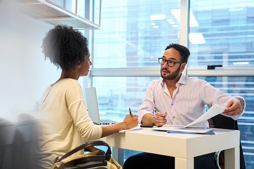 Medium shot of adult male financial advisor discussing with African American female customer while sitting in office during daytime