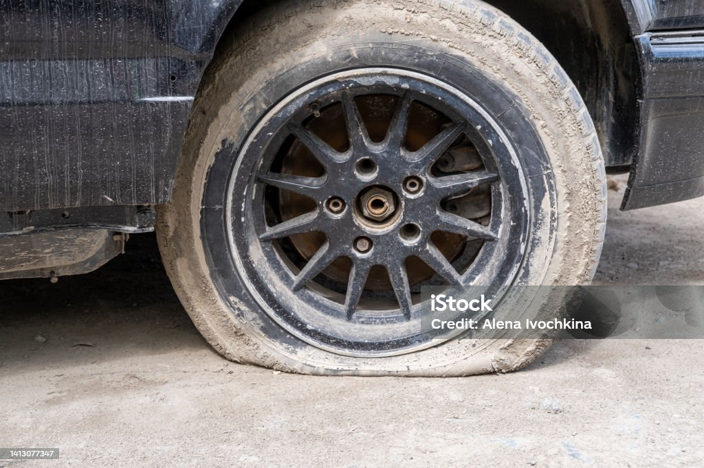 Close-up Of A Damaged Flat Tire Of A Car On The Road. Old wheel car dirty and flat tires. Car tire puncture. Close-up Of A Damaged Flat Tire Of A Car On The Road. Old wheel car dirty and flat tires. Punctured wheel of a modern car on the road. Car tire puncture. Car Stock Photo