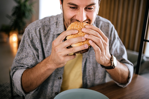 Young businessman having a lunch break and eating burgers while telecommuting from home