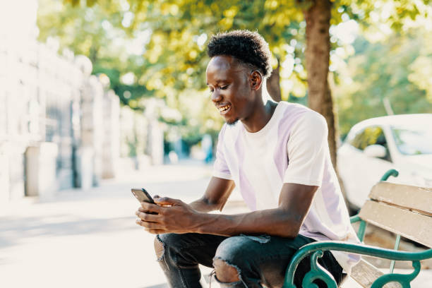istock Young African male using smart phone while sitting on the bench outdoors 1413078016
