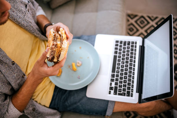 Man eating hamburger while working on laptop