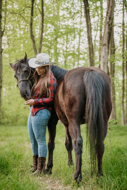 istock Young cowgirl feeding her horse while standing against trees at forest 1413078975