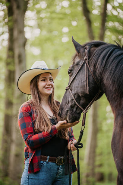 istock Smiling young cowgirl feeding her horse while standing at forest 1413079053