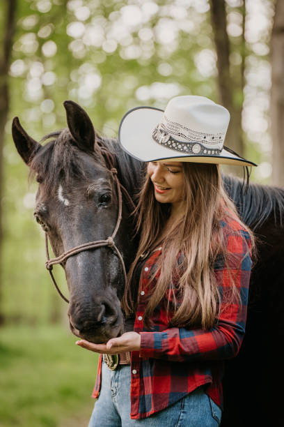 istock Happy young cowgirl feeding her horse while standing at forest 1413079140