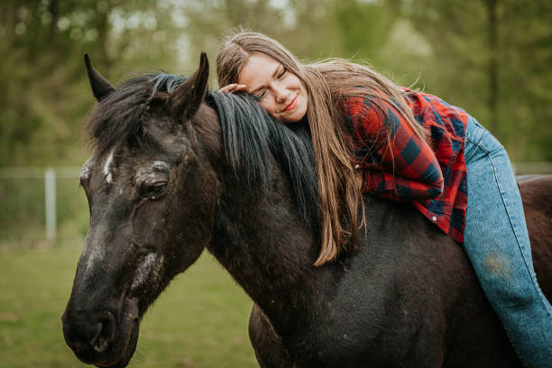 istock Smiling woman embracing horse while riding in ranch against trees 1413079293
