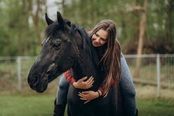 istock Smiling young woman embracing horse while riding in ranch 1413079502