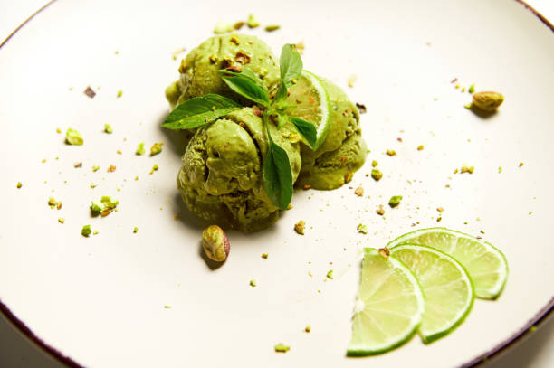 Close-up scoops of pistachio sorbet ice cream with lemon basil on a white plate, garnished with fresh juicy lime slices