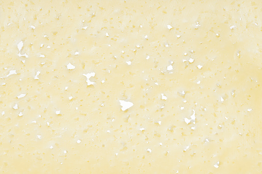 Background texture for design from a yellow piece of cheese with numerous holes.