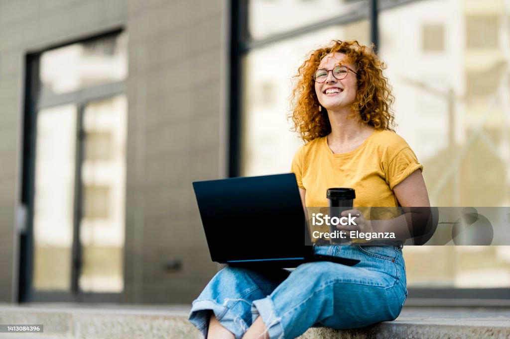 Young redhead woman working on laptop in the city Yellow Stock Photo