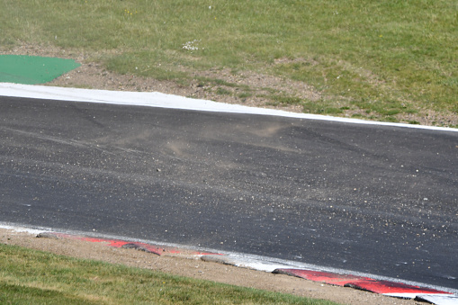 A stretch on an asphalt grey race track highlighted by red and white chevrons, clear dark grey skid marks indented on the race track and specked of gravel over the racetrack